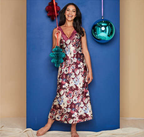 A woman standing tall, wearing a floral nightgown, holding Christmas decorations.