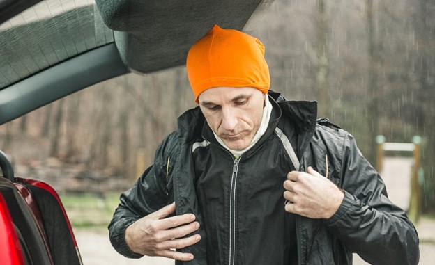 An older man putting a waterproof coat on before stepping out into the rain.