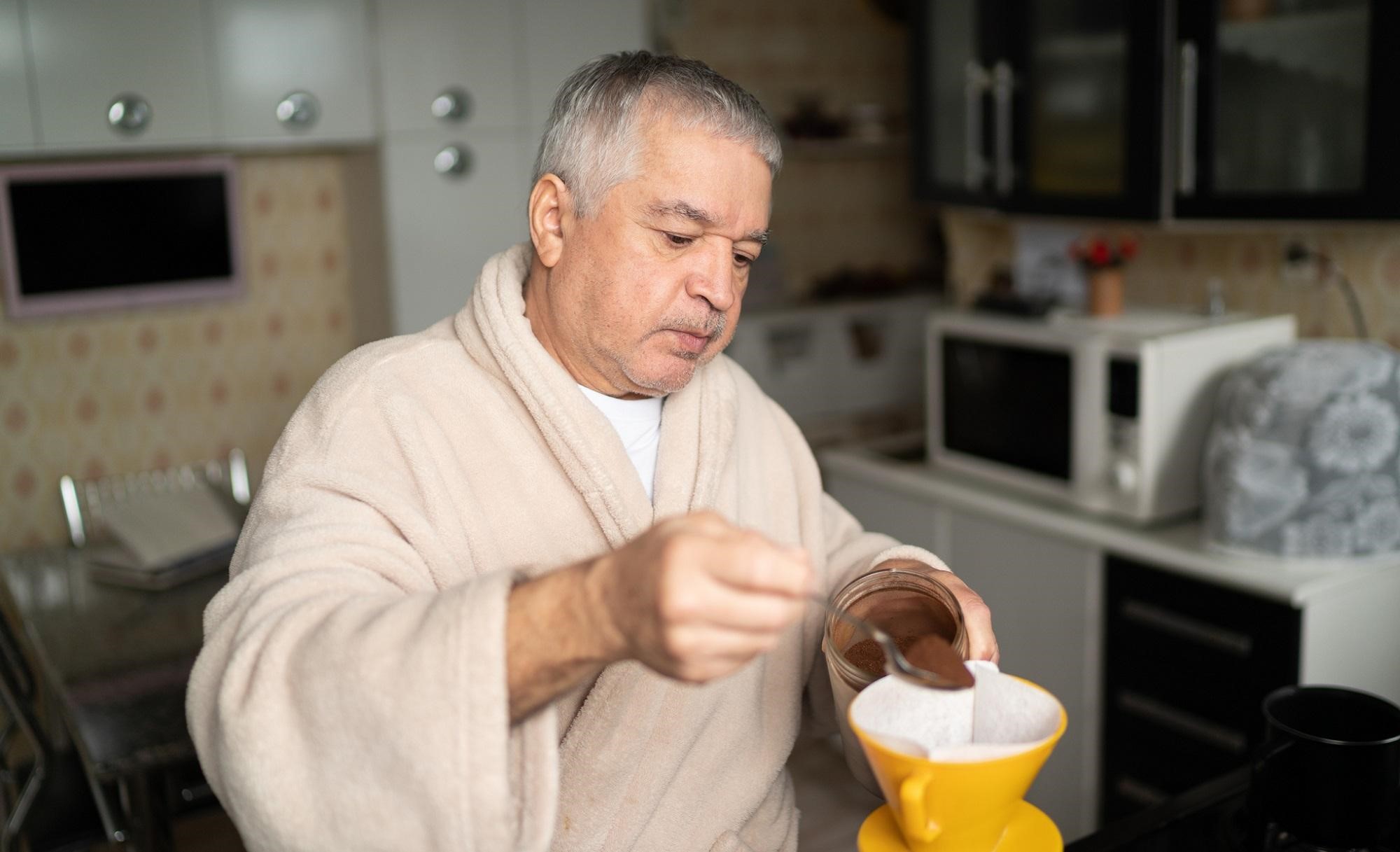 An older man in a bathrobe making coffee.