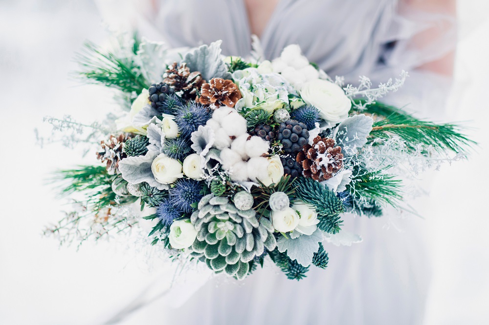 a winter bride holds a green, white and blue floral bouquet