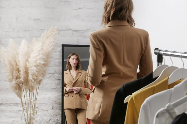 A woman tries on coordinating trousers and jacket combination in front of a mirror.