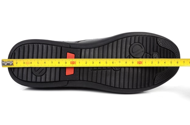 a man’s shoe lying on its side with a tape measure running across its sole
