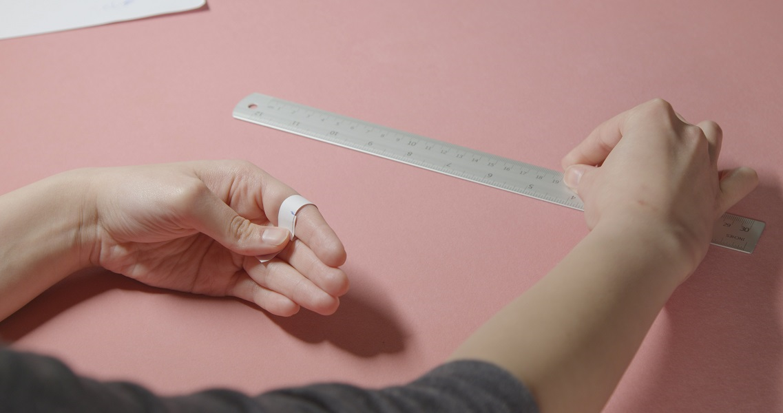 A woman measuring her ring size using paper and a ruler.