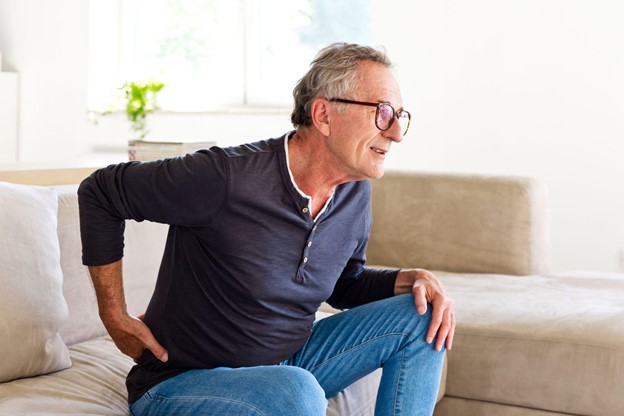 A pile of knita man sitting down on a sofa holding is lower back in discomfortwear