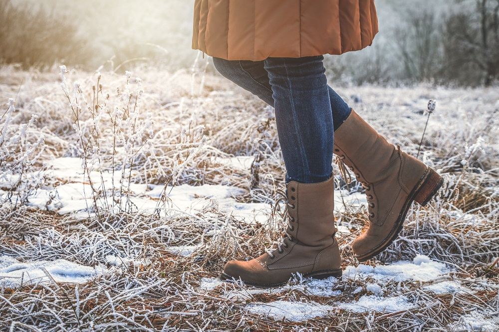 A woman walks through a snowy, frosty field wearing a winter coat, winter boots and jeans.