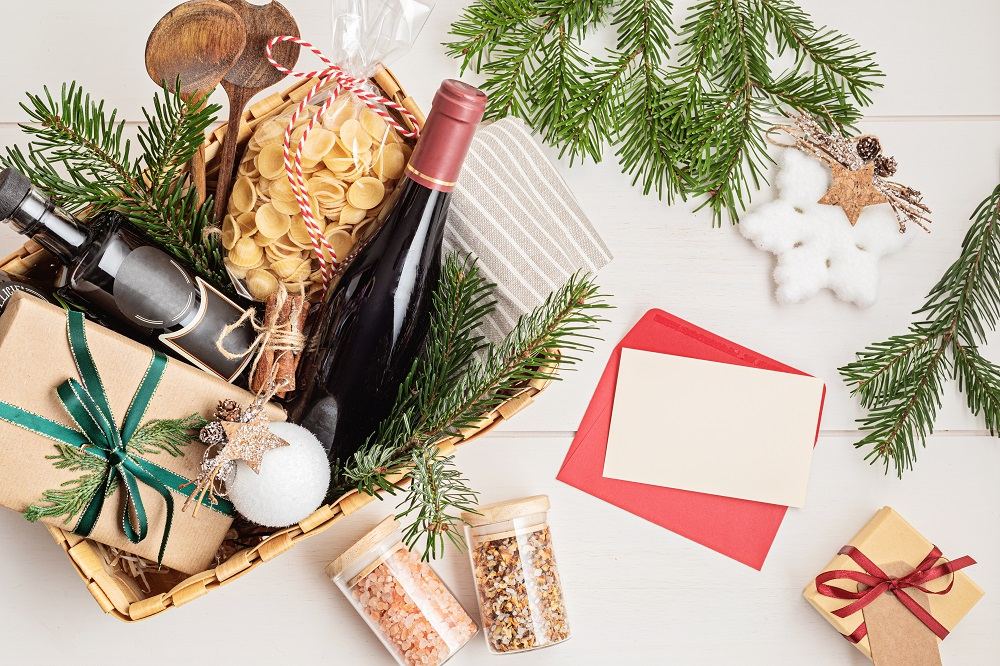 A Christmas food and drinks hamper on a tabletop, next to a wrapped present and card.