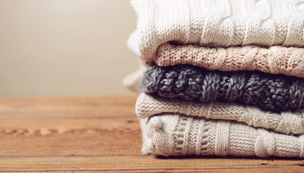 A set of knitted jumpers piled up on a table.