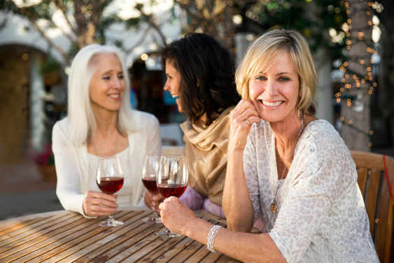 Image alt text: mature woman in a patterned blouse drinking wine with her friends