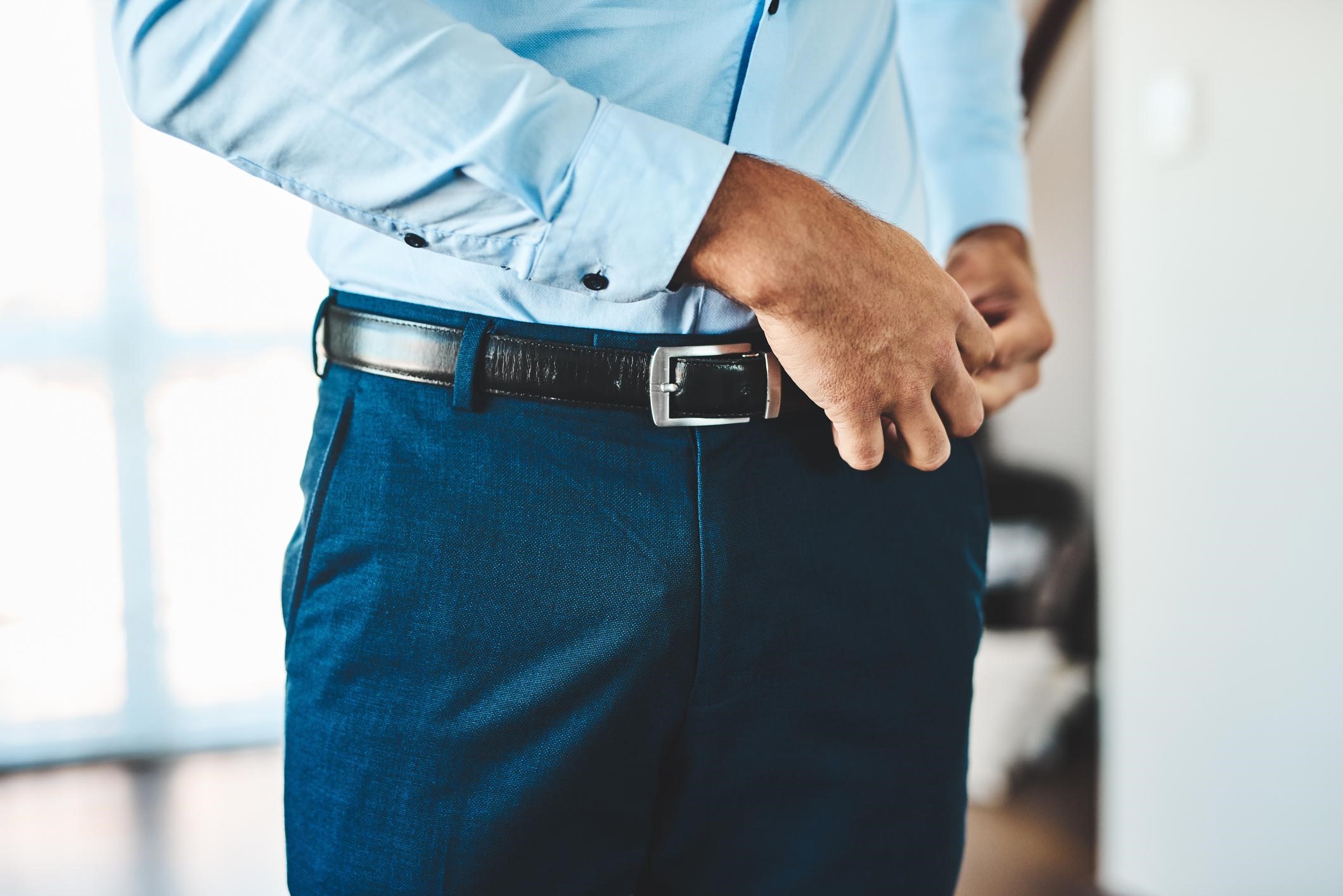 man doing his suit trousers up with a belt