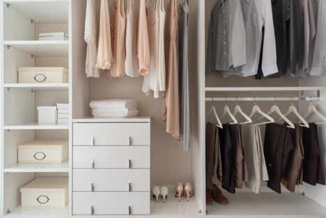 a large built in wardrobe with pastel-coloured women's clothes on one side and grey and brown men's clothes on the other